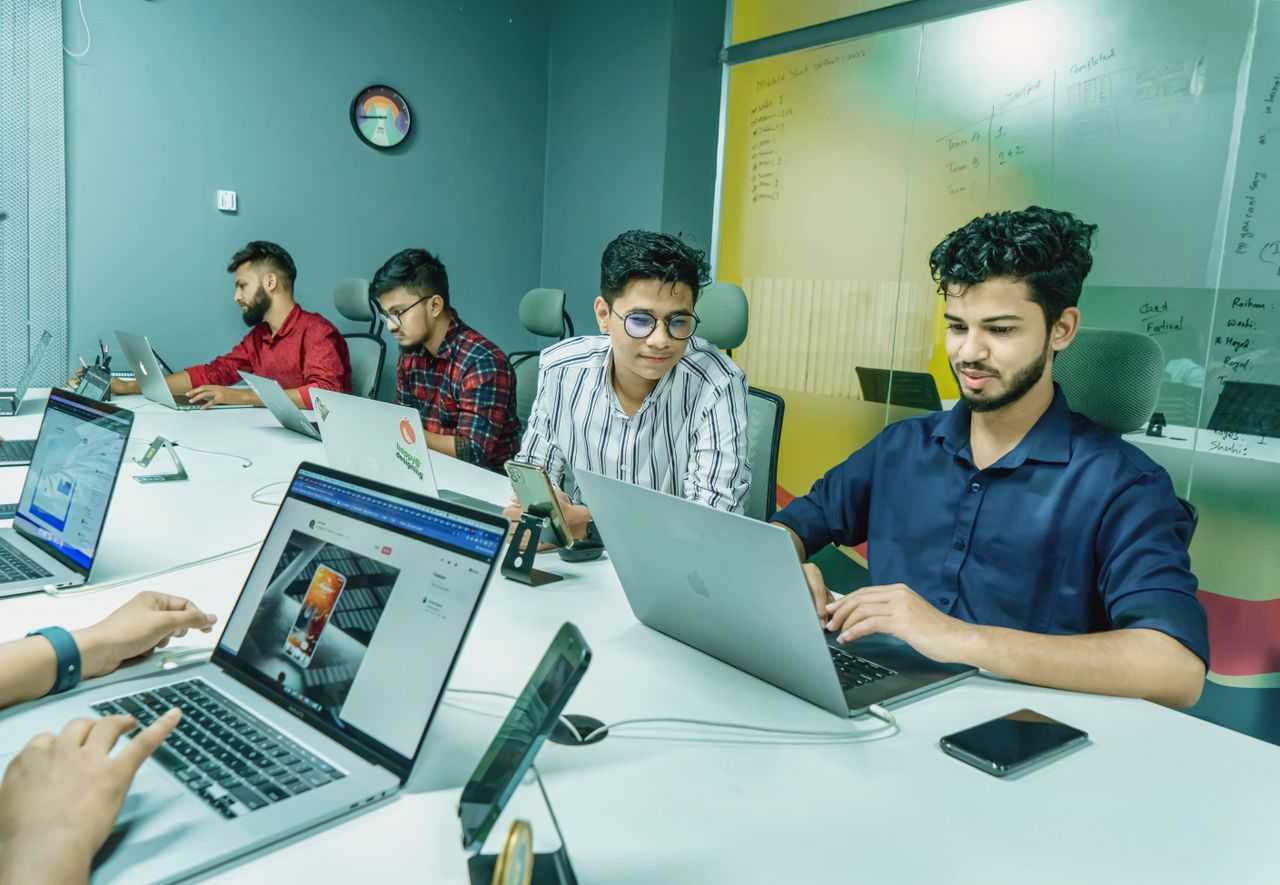 Group of young professionals working together in a modern office setting, using laptops and technology.